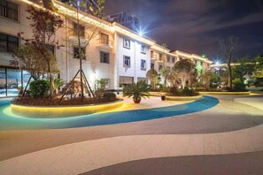 A hotel courtyard with a swimming pool, potted plants, and a well-lit building facade. - Meilan Hot Spring Hotel (Anshun)