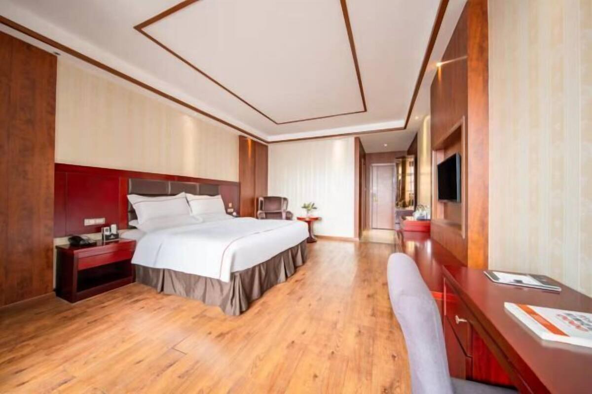 Ein Hotelzimmer mit einem großen Bett, einem Schreibtisch, einem Sessel, einem Fernseher und einem kleinen Tisch mit einer Pflanze.