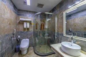Un baño con ducha envuelta en vidrio, un inodoro y un lavamanos con espejo arriba.