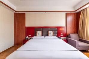 Habitación de hotel con una cama grande, cabecera roja, dos mesitas de noche con lámparas y una silla.