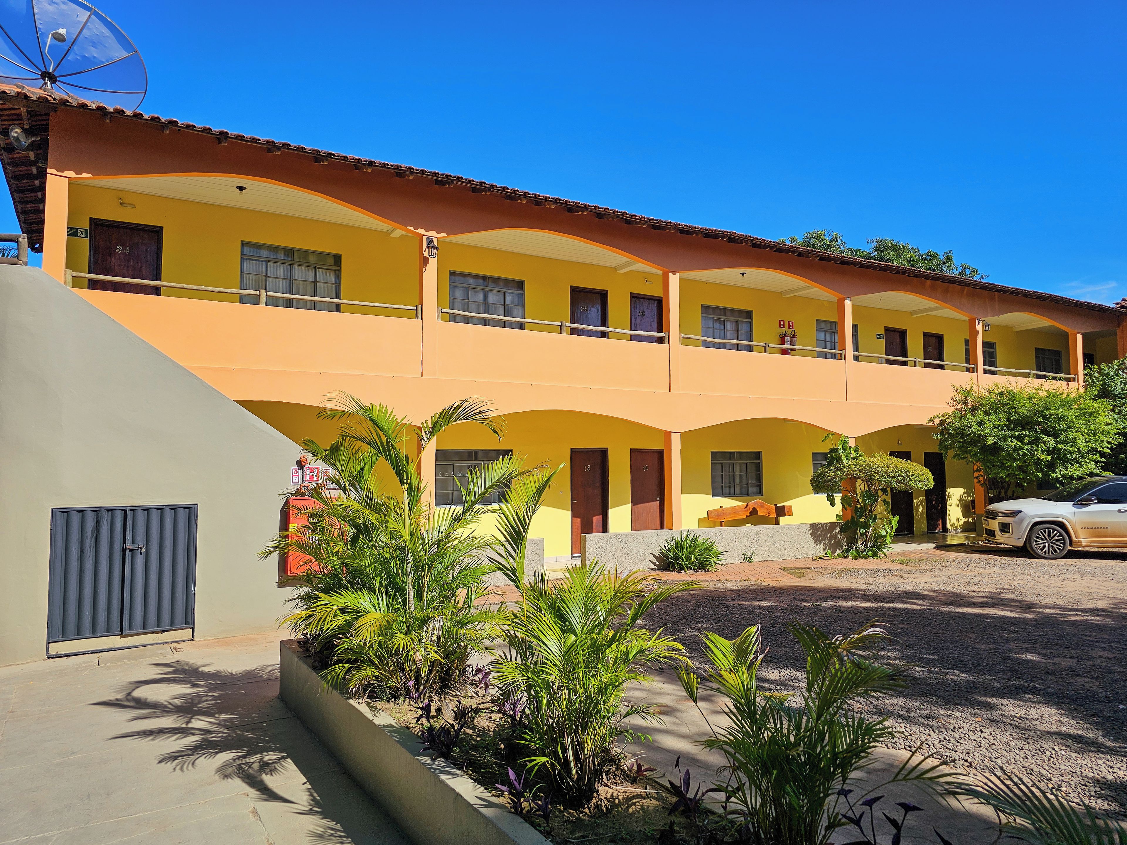 A multi-story building with a yellow facade, multiple balconies, and a parking area with a car.