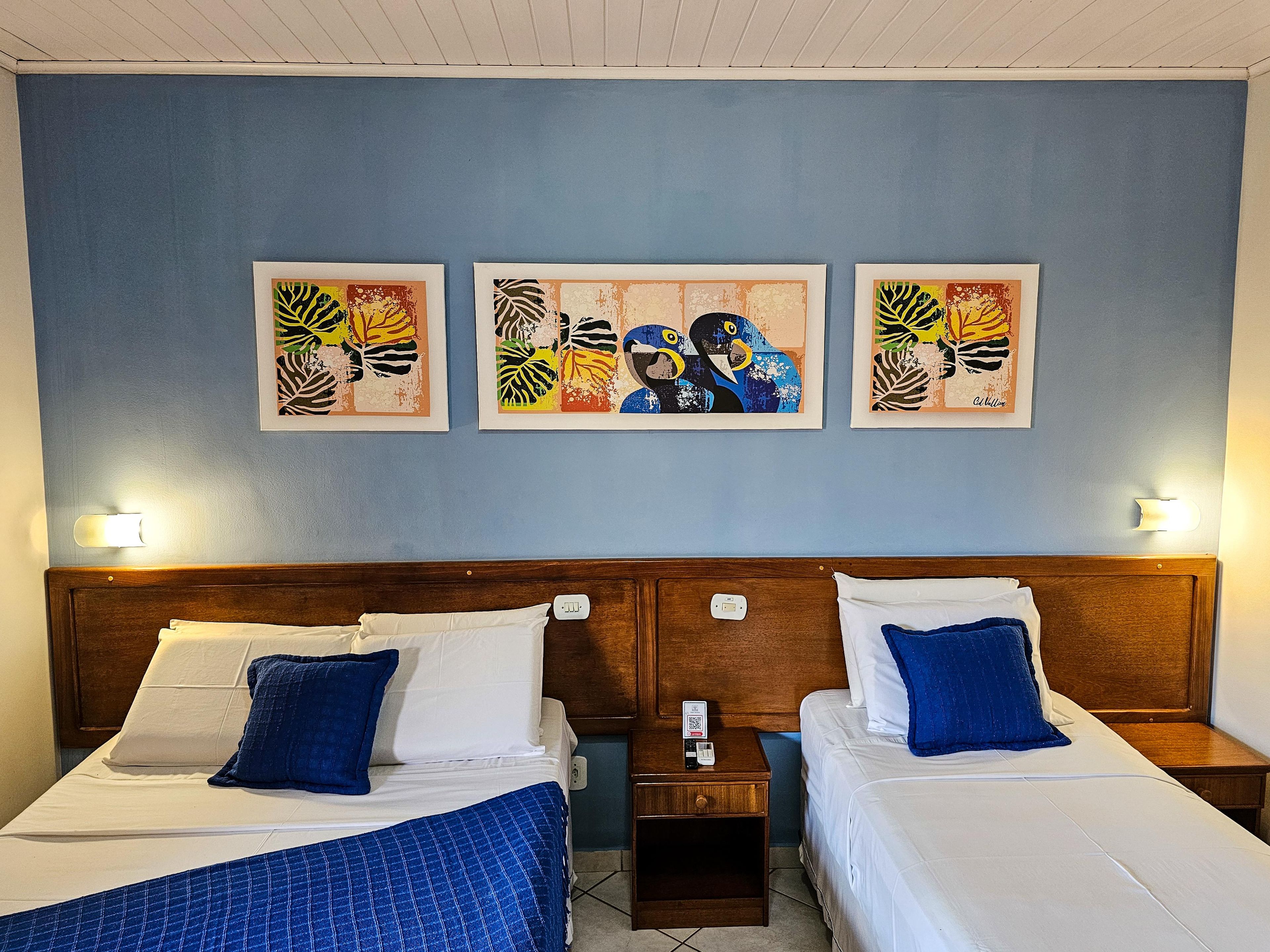 A hotel room with two beds, a nightstand, a wall-mounted light, and three framed artworks.