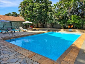 A swimming pool with a stone border, surrounded by lounge chairs and umbrellas. - Pantanal Hotel (Miranda)