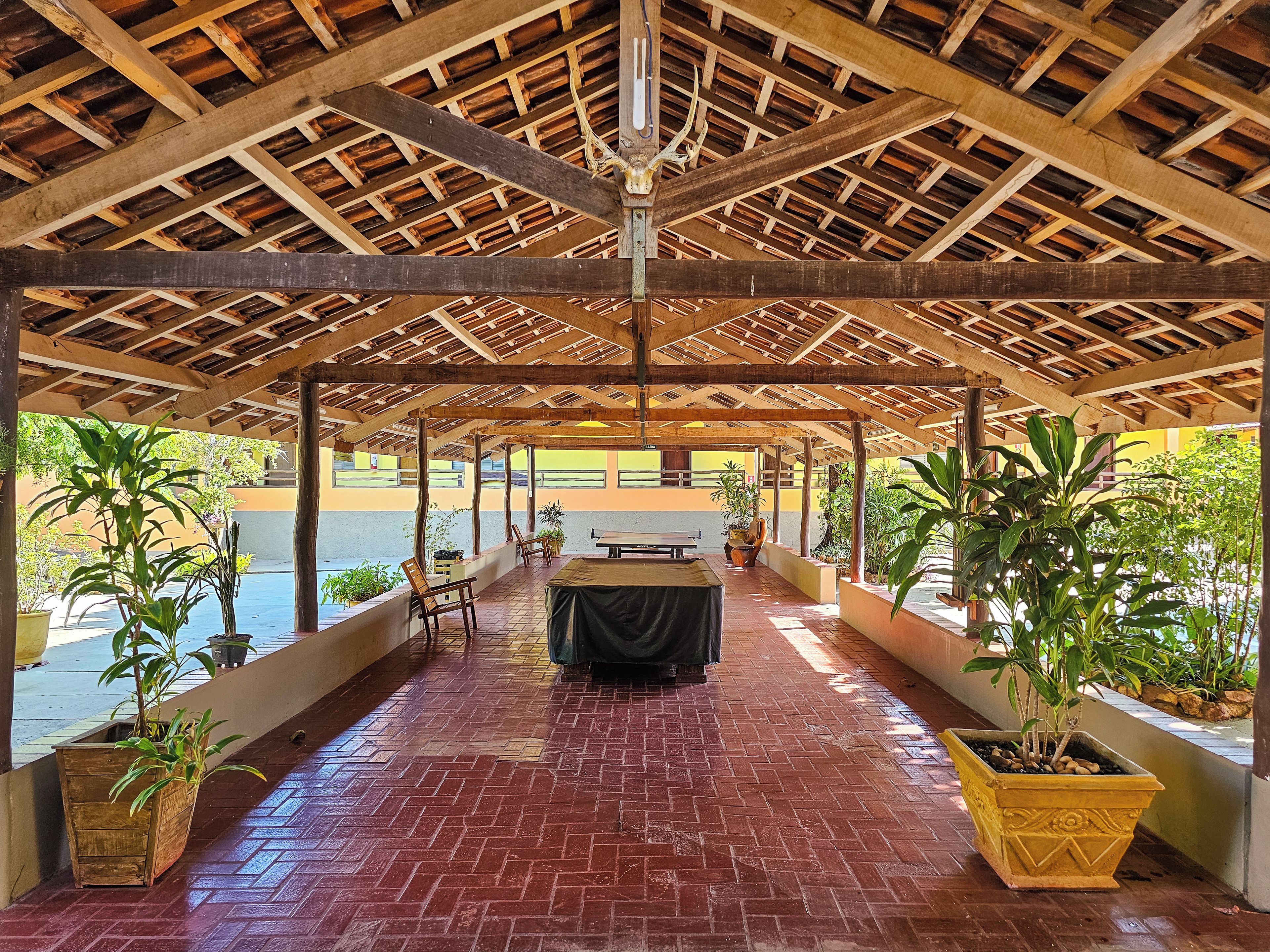 A covered outdoor area with a brick floor, wooden beams, and potted plants.