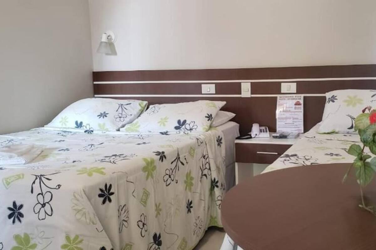 Habitación de hotel con dos camas, una mesita de noche, una pequeña mesa con una planta en maceta y lámparas fijadas a la pared.