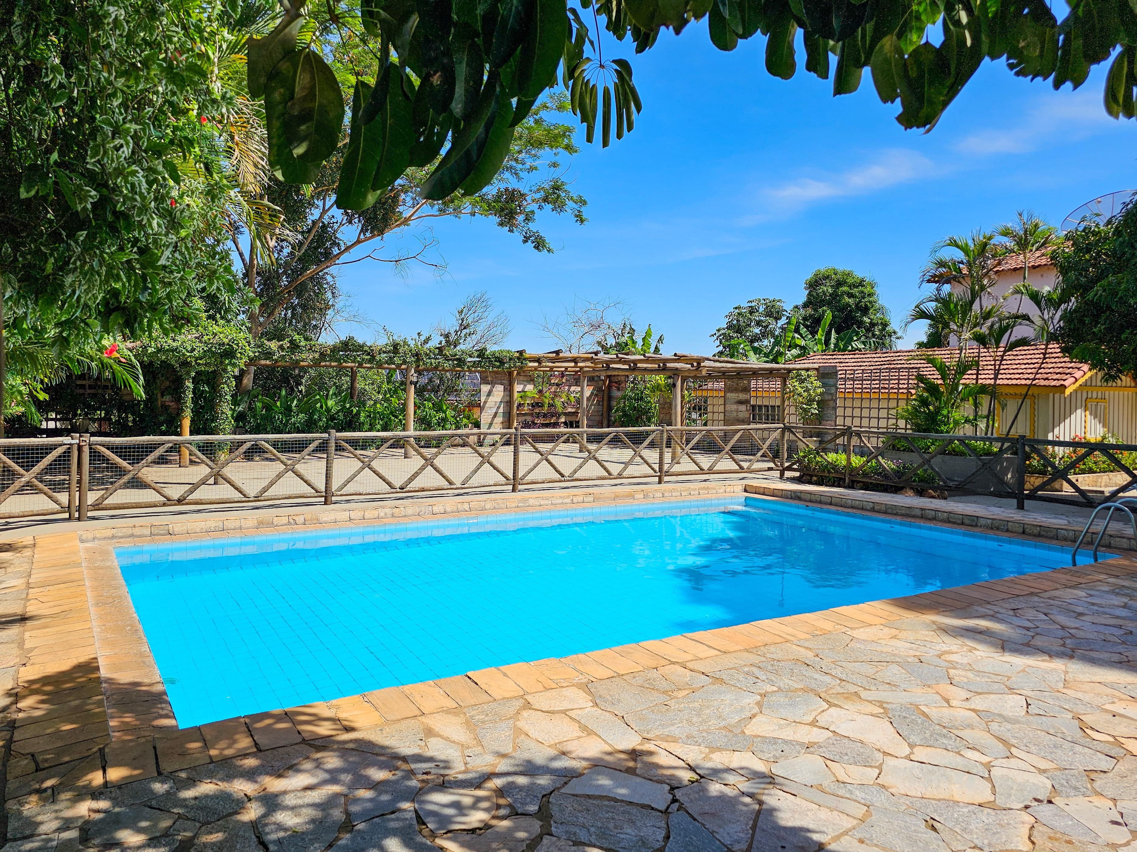 A swimming pool with a stone deck, surrounded by a wooden fence and lush greenery.