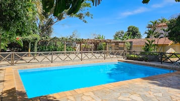 A swimming pool with a stone deck, surrounded by a wooden fence and lush greenery.