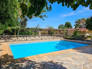 A swimming pool with a stone deck, surrounded by a wooden fence and lush greenery. - Pantanal Hotel (Miranda)