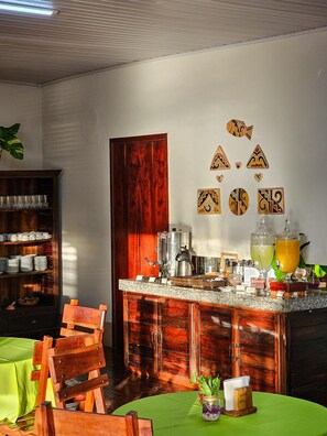 A hotel room with a wooden cabinet, a green table, and a bar area with a coffee machine and drinks. - Pantanal Hotel (Miranda)
