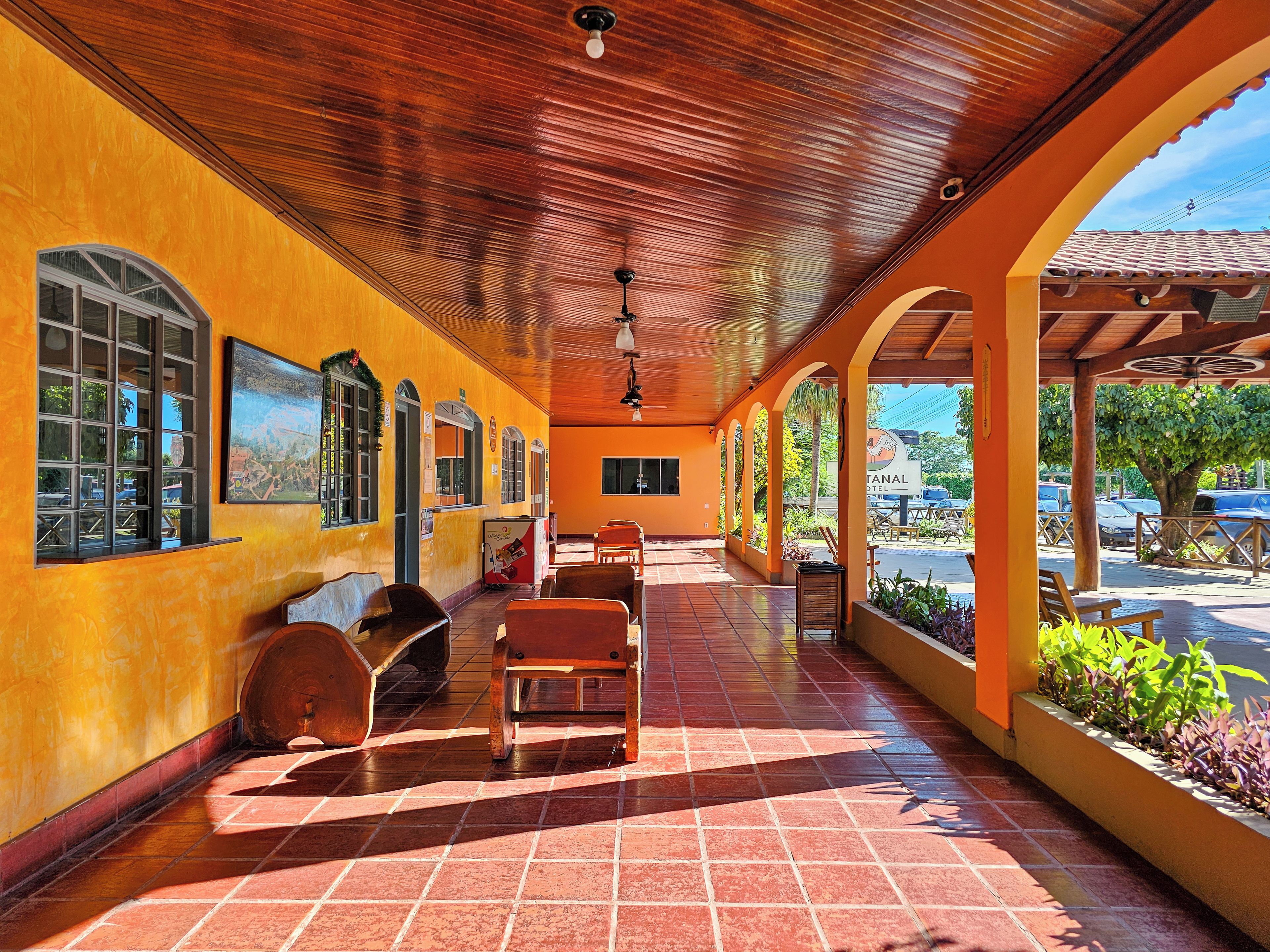 A covered outdoor area with wooden benches and a tiled floor, featuring a view of a street and parked cars.