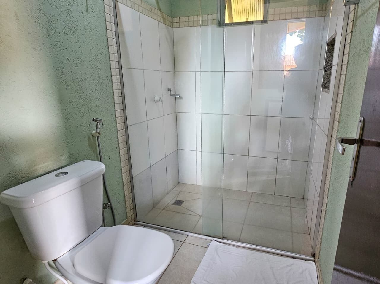 Casa de banho com sanita, cabine de duche e porta de vidro.