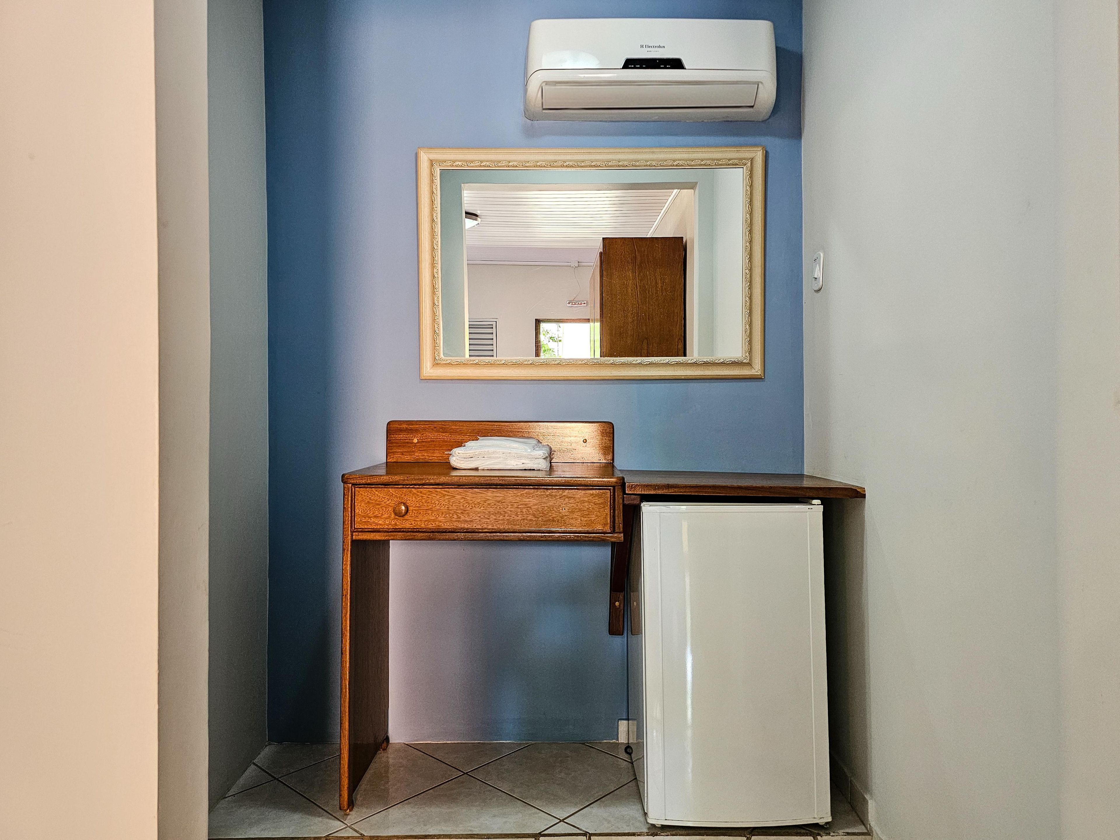 Ein Badezimmer mit einem Holzkosmetikschrank, einem Spiegel, einem weißen Kühlschrank und einer Wandklimaanlage.