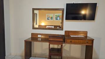 Quarto com escrivaninha de madeira, cadeira, espelho e televisão de tela plana fixada na parede.