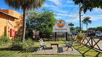 Placa do Hotel Pantanal com logotipo, cercada por vegetação e área pavimentada com bancos.