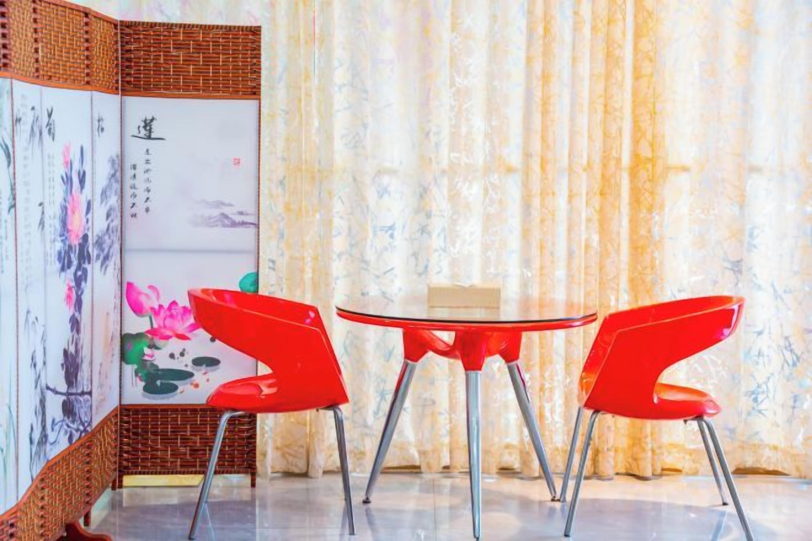 A room with a traditional Chinese screen, a round table, and two red chairs.