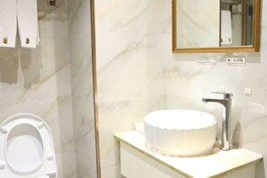 A bathroom with a toilet, a sink with a marble countertop, and a mirror with a gold frame.