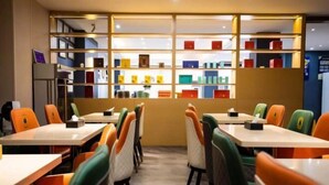 A restaurant with tables and chairs arranged in rows, a wall with shelves displaying various items, and a counter area. - Super 8 Hotel (Xiamen Tong'an Bell Tower) (Xiamen)