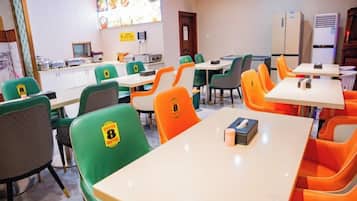 A dining area with tables and chairs, a kitchen counter, and a refrigerator.