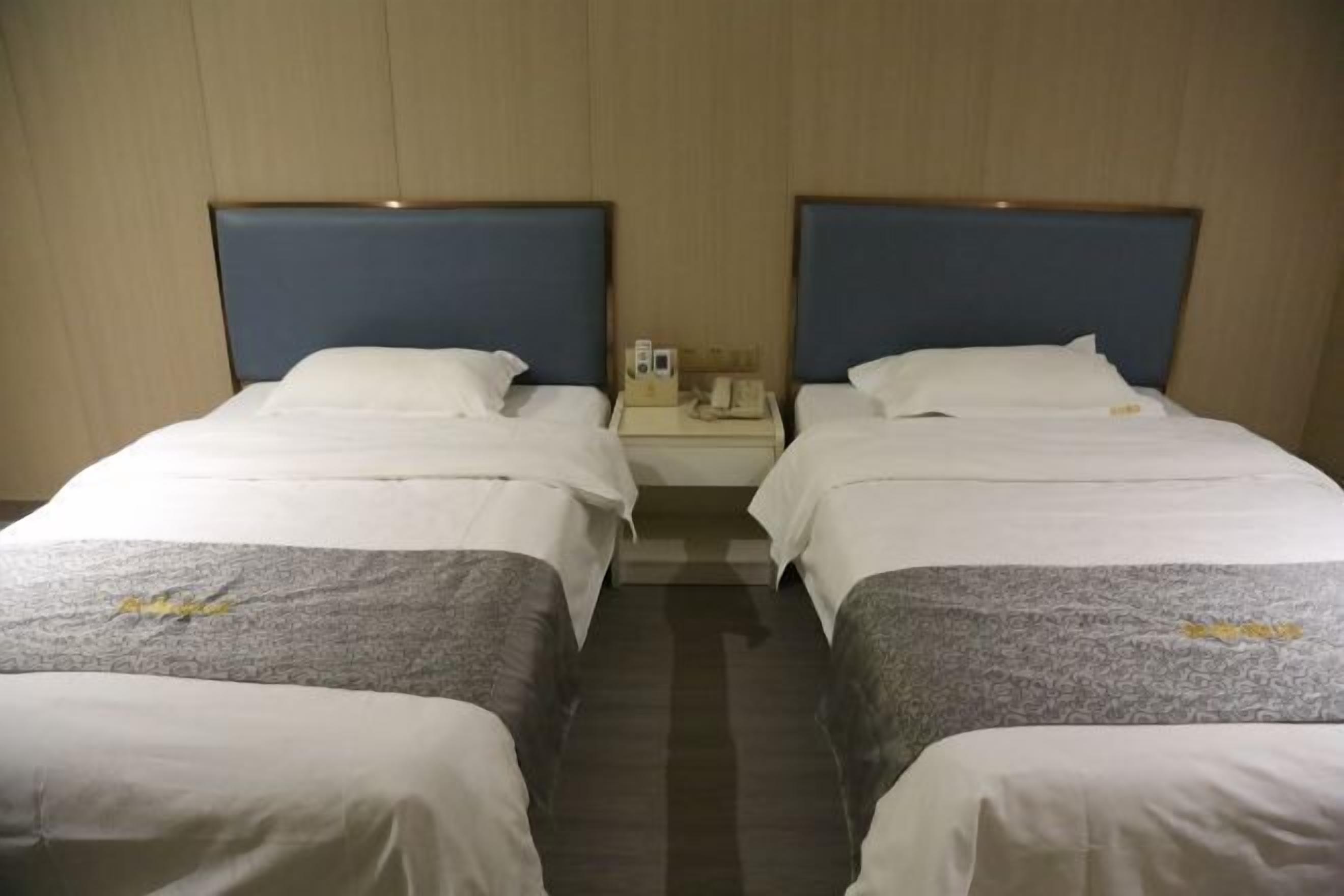 A hotel room with two single beds, a nightstand with a phone and a lamp, and a wooden headboard.