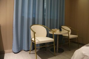 A hotel room with a bed, two white chairs with gold frames, a small round table, and a blue curtain. - Super 8 Hotel (Xiamen Tong'an Bell Tower) (Xiamen)