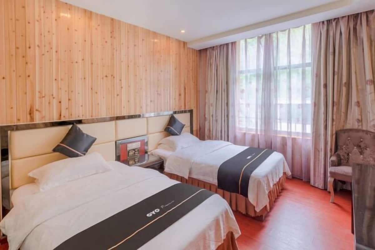 Een hotelkamer met twee bedden, houten lambrisering, een groot raam met gordijnen en een stoel.