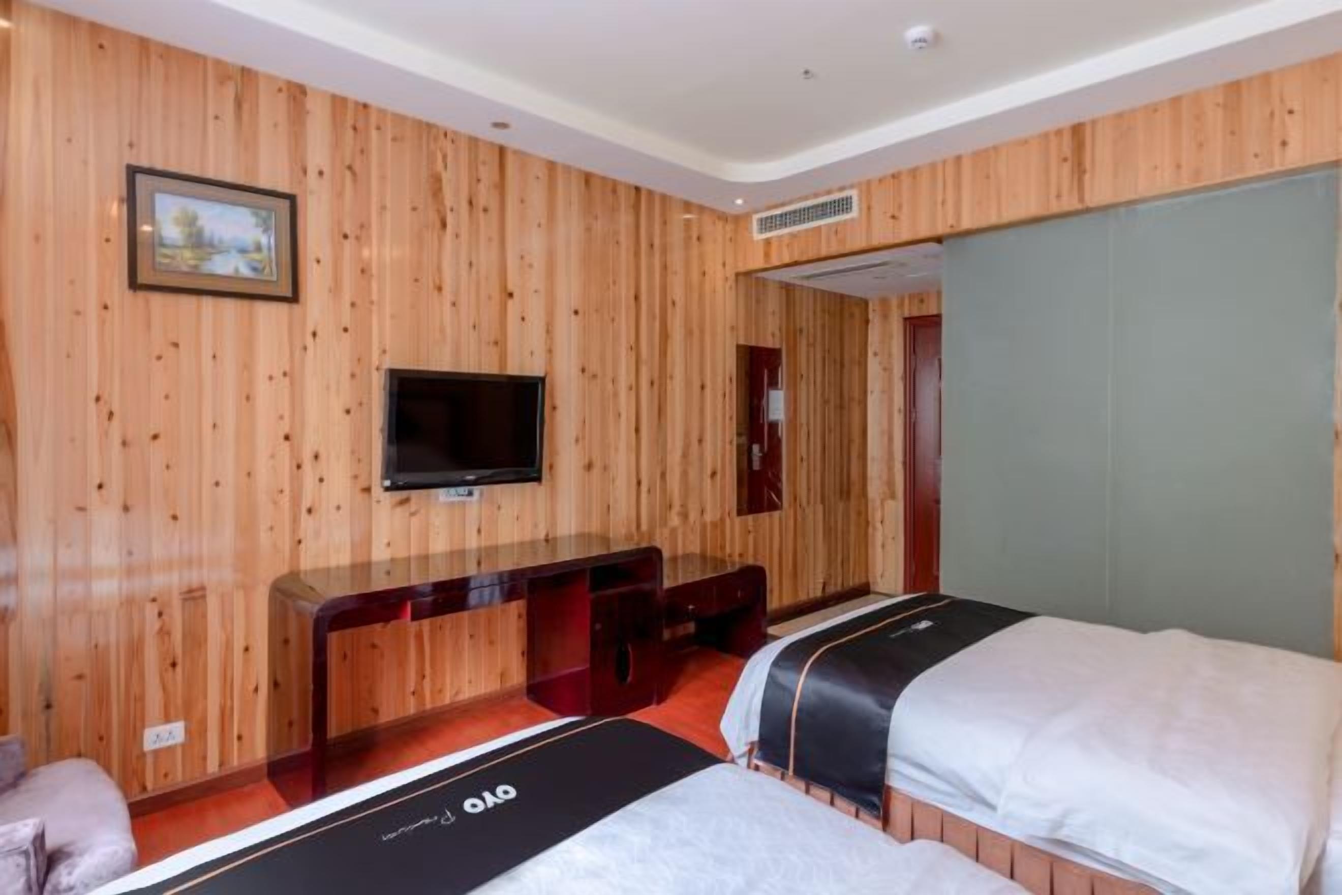 A hotel room with wooden panel walls, a flat-screen TV, a desk, and two beds.