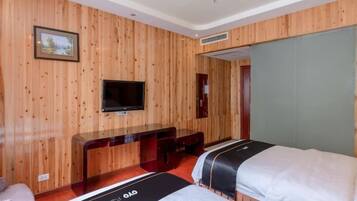 A hotel room with wooden panel walls, a flat-screen TV, a desk, and two beds.