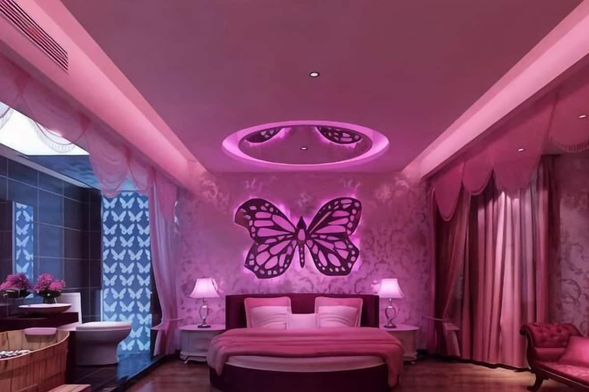 Een slaapkamer met een grote wanddecoratie van een vlinder, een bed, bedlampen, een kaptafel met spiegel en een raam met gordijnen.