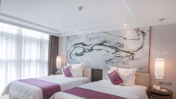 Een hotelkamer met twee bedden, een marmeren wanddecoratie en een groot raam met gordijnen.