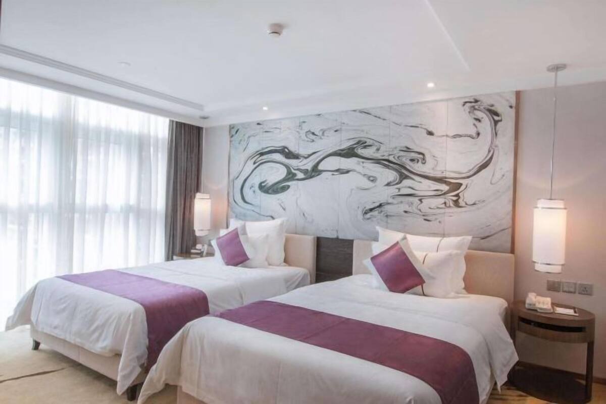 Een hotelkamer met twee bedden, een marmeren wanddecoratie en een groot raam met gordijnen.