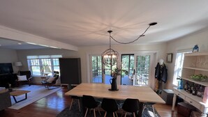 A spacious living room with a wooden dining table, black chairs, a large TV, and a fireplace.