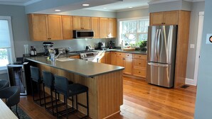 A modern kitchen with wooden cabinets, a stainless steel refrigerator, a microwave, and a large island with bar stools.