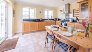 A spacious kitchen with wooden cabinets, a large island with seating, and a view of the outdoors. - Culver House, Aldeburgh (Aldeburgh)