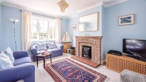 A living room with a blue sofa, a fireplace, a television, and a large window. - Culver House, Aldeburgh (Aldeburgh)