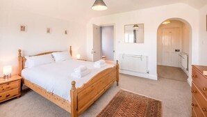 A bedroom with a wooden bed, a nightstand, a mirror, a radiator, and a dresser. - Culver House, Aldeburgh (Aldeburgh)