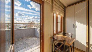 Varanda com vista para o céu e nuvens, mesa de madeira com cadeiras, e um guarda-roupa branco.