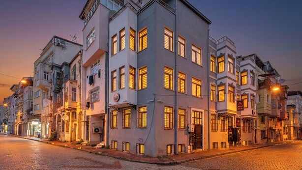 Um edifício de vários andares com várias janelas e varandas, uma rua de paralelepípedos e um céu claro.