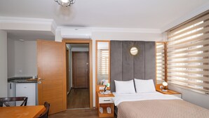 Quarto de hotel com cama, mesa de cabeceira, luminária e pequena escrivaninha com cadeira.