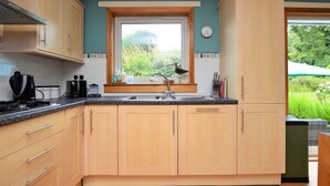 A kitchen with wooden cabinets, a window with a view of greenery, and a sink with a faucet. - Brookfield, picturesue quiet location, sleeps 8, pet friendly (Dunoon)