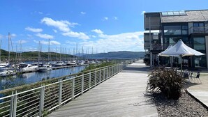 A marina with boats docked, a wooden walkway, and a modern building with outdoor seating. - Brookfield, picturesue quiet location, sleeps 8, pet friendly (Dunoon)