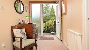 A hallway with a wooden chair, a dresser, a mirror, and a door leading to a balcony with a view of greenery. - Brookfield, picturesue quiet location, sleeps 8, pet friendly (Dunoon)