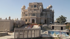 Un grande edificio decorato con numerose cupole e balconi, un’area piscina con lettini e un’elaborata struttura giardino.