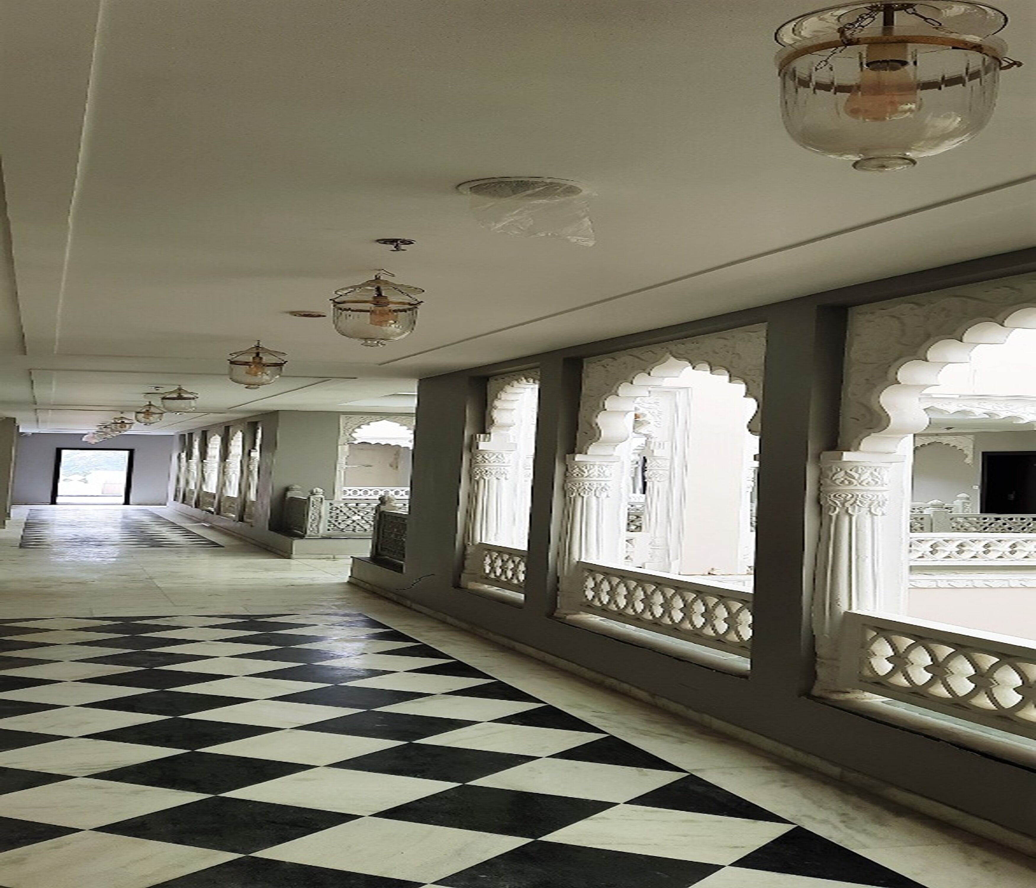 A corridor with patterned flooring and ornate windows with intricate designs.