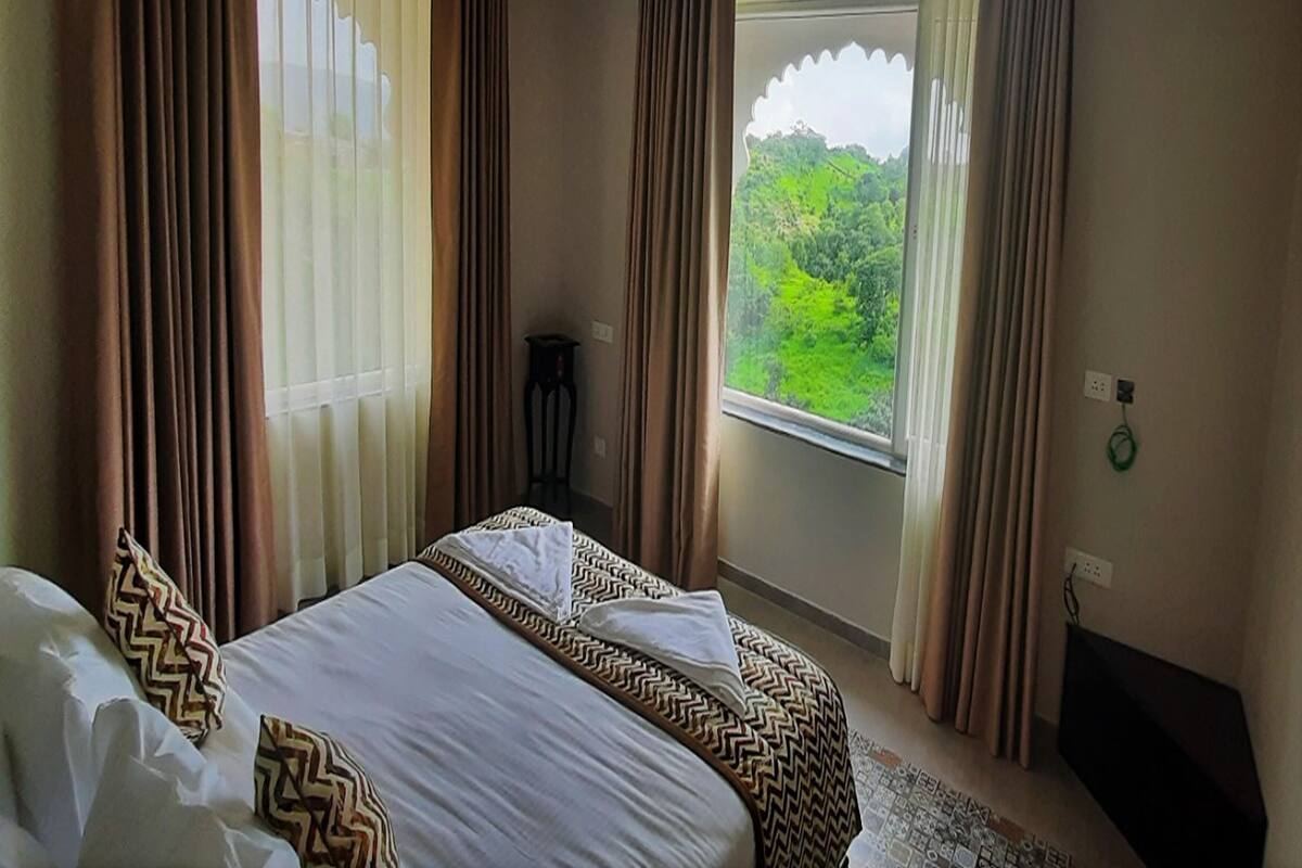 Una habitación de hotel con dos camas, vistas al verdor exterior y una mesita.