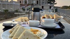 Un tavolo imbandito con panini, patatine fritte e una bevanda calda, con sullo sfondo un edificio storico.