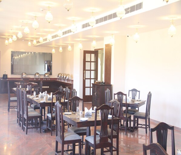 Un espace repas comprenant plusieurs tables et chaises, un grand miroir et un plafond orné de luminaires suspendus.
