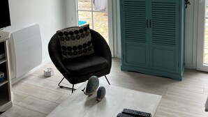 A living room with a black armchair, a teal cabinet, and a TV on a stand. - Maison Centre-ville Avec Jardin (Châtelaillon-Plage)