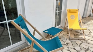 Two folding chairs with wooden frames and fabric seats, one blue and one yellow, positioned on a stone-tiled patio. - Maison Centre-ville Avec Jardin (Châtelaillon-Plage)