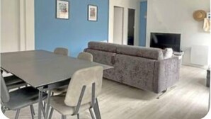 A modern living room with a grey sofa, a dining table with chairs, and a flat-screen TV. - Maison Centre-ville Avec Jardin (Châtelaillon-Plage)