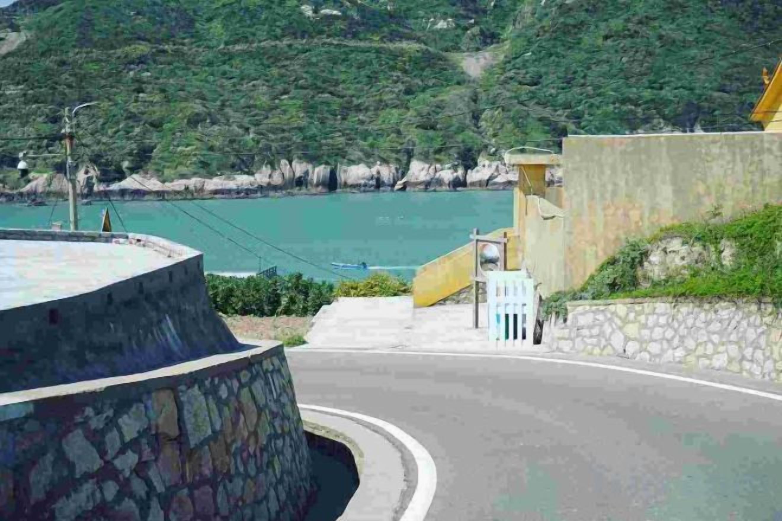 Una carretera costera con un muro de piedra, un edificio amarillo y vistas al mar.